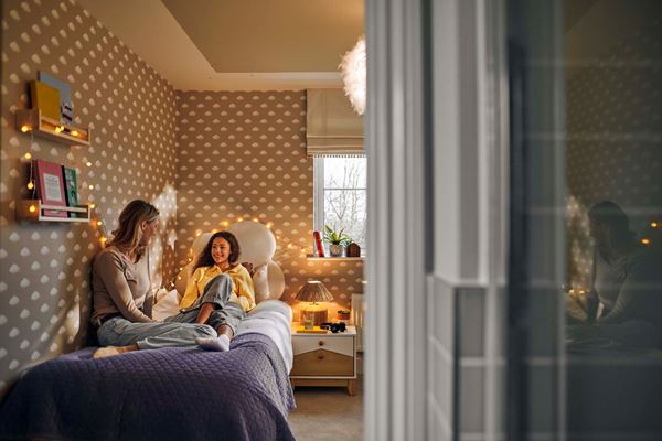 A mother talking to her child in a modern bedroom of a Charles Church home with cloud wallpaper.