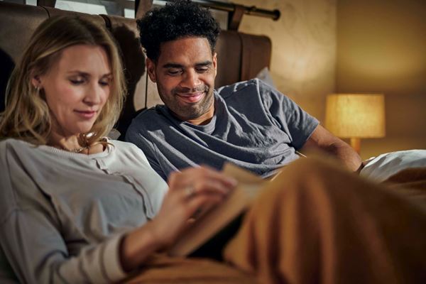 A happy couple lying in a bed reading a book.