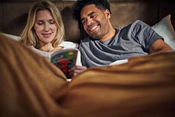 A happy couple sat up in bed reading a book.