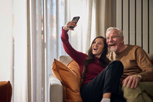 Young woman taking selfie with father in new home while sitting on a sofa.