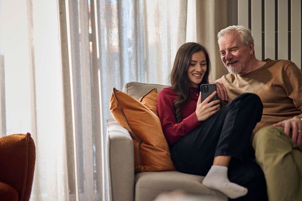 A daughter and a father looking at a mobile phone while sat in a modern living room.