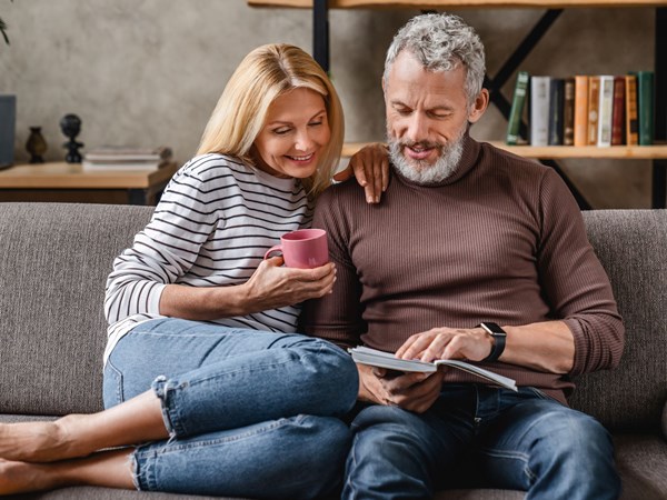 A couple sat on a sofa looking at a book together.