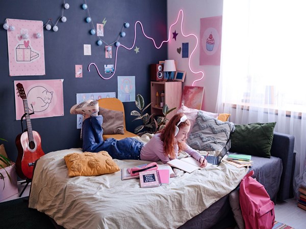 A teen sat on her bed writing in a notepad and looking at a laptop. 