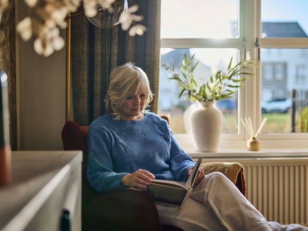 An older woman in a blue jumper reading a book.